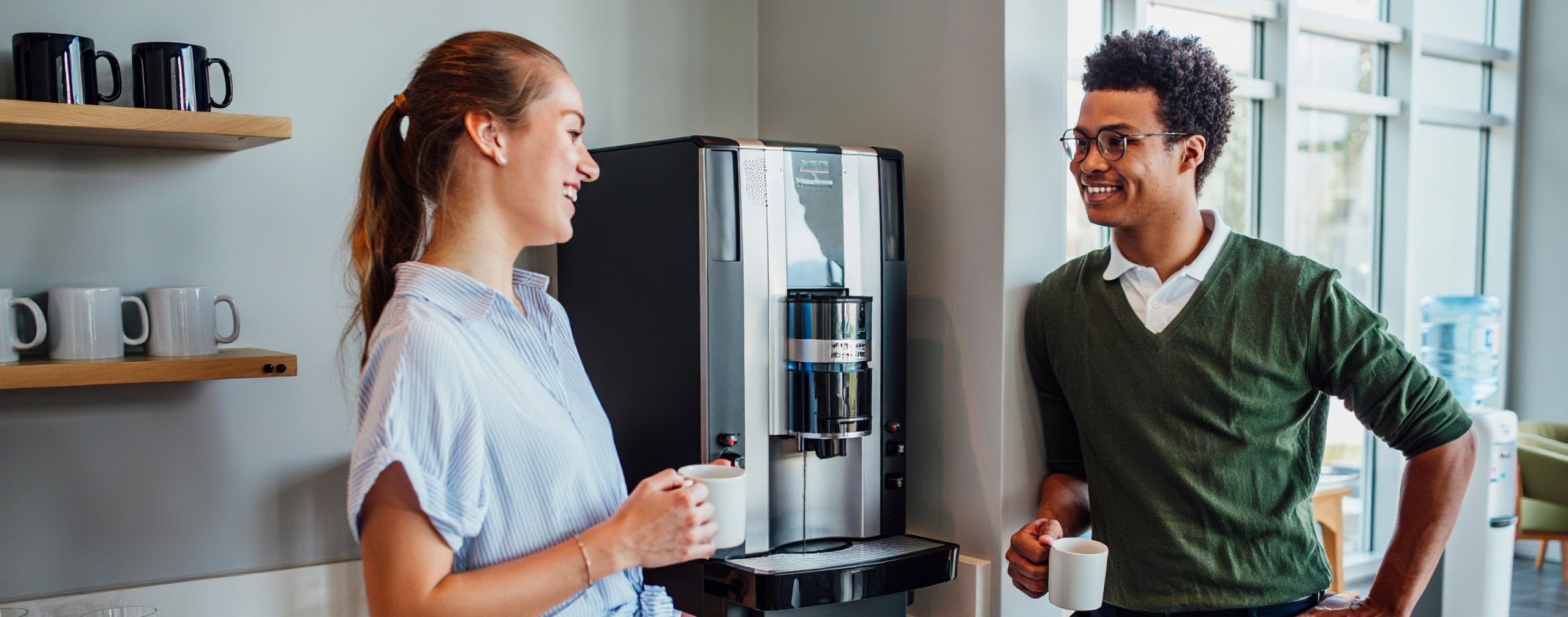Zwei Arbeitskollegen tratschen an der Kaffeemaschine.